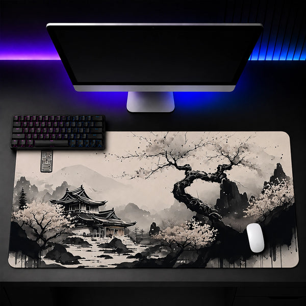 A large rectangular desk mat with a black and white traditional landscape print featuring a pagoda, flowering trees, and misty mountains, shown on a desk beneath a computer monitor, keyboard, and mouse.